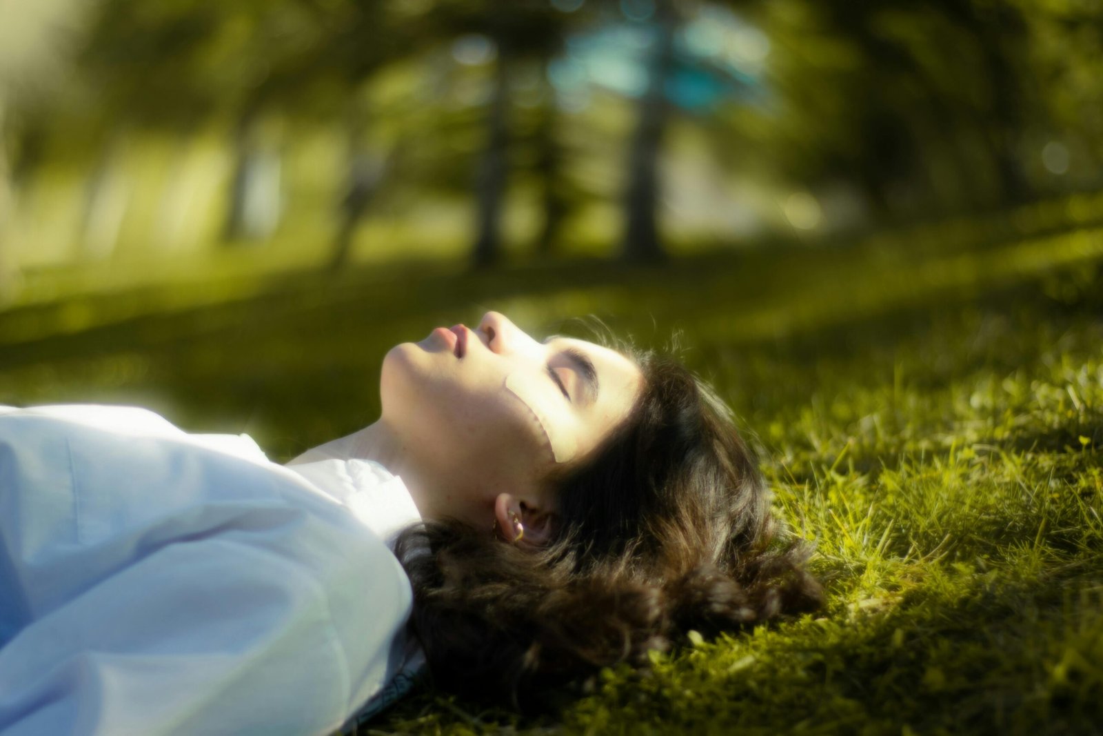 A serene portrait of a woman lying down on grass, eyes closed and relaxed in nature.